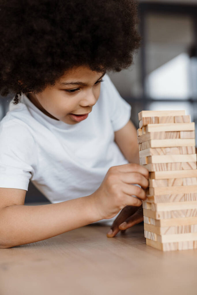 Black curly boy playing with wooden planks at home - Photo, Image