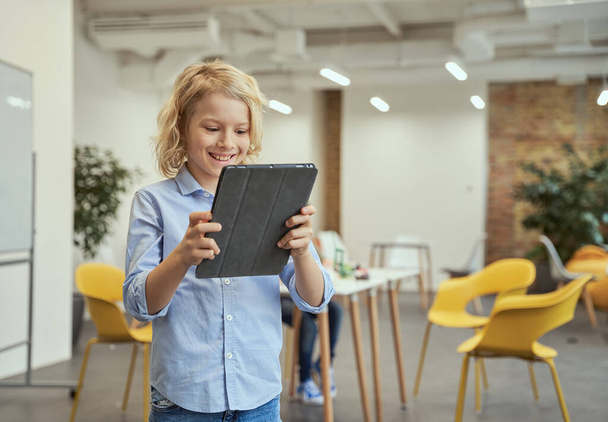 Portret van een lachend jongetje met tablet-pc terwijl hij poseerde voor de camera tijdens STEM-lessen - Foto, afbeelding