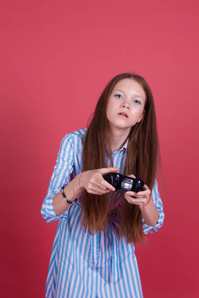 Little kid girl 13 years old in blue dress isolated on pink background holding joystick gaming serious concentrated playing games - Foto, Imagen