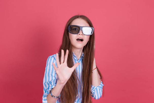 Niña 13 años de edad en vestido azul con soportes aislados sobre fondo rosa con gafas de cine 3d impactados - Foto, imagen