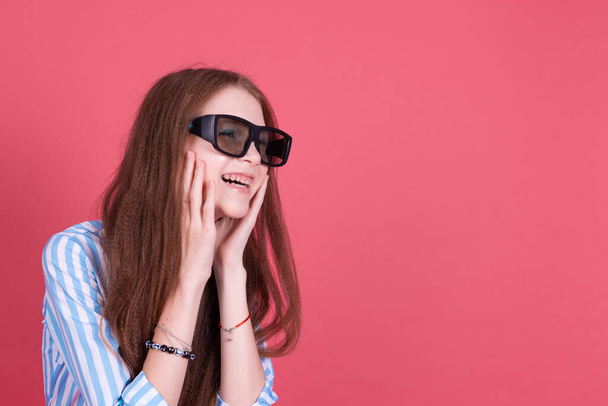 Menina criança 13 anos de idade em vestido azul com suportes isolados no fundo rosa vestindo óculos de cinema 3d feliz sorrindo rir - Foto, Imagem