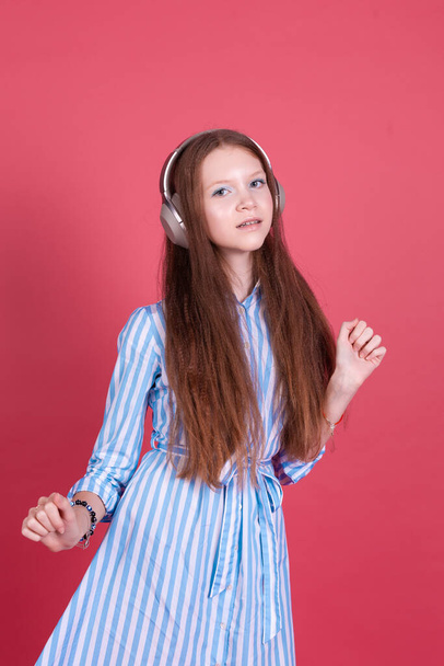 Little kid girl 13 years old in blue dress with brackets isolated on pink background in wireless headphones happy smiling dancing moving - Фото, зображення