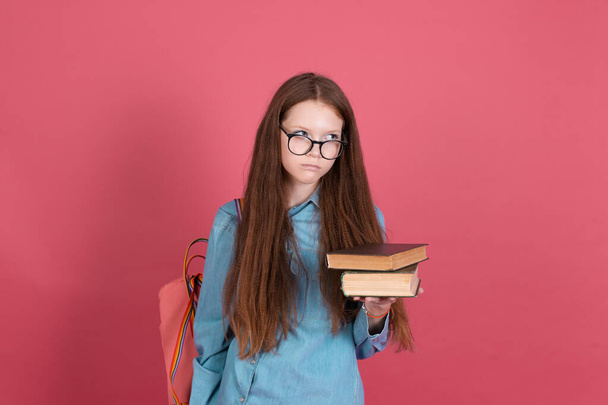 13 yaşında küçük bir kız çocuğu pembe arka planda izole edilmiş sırt çantalı ve kitaplı bir kız çocuğu mutsuz bir şekilde çalışmaktan nefret ediyor. - Fotoğraf, Görsel