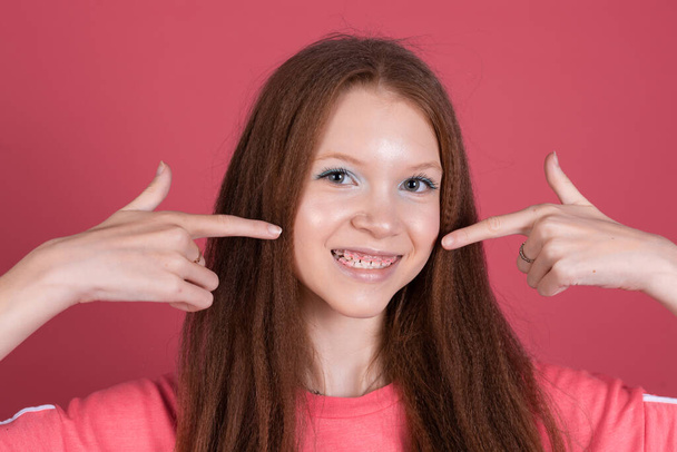 13歳の女の子子供でカジュアル隔離されました上のテラコッタ背景幸せなポイント指上の白い歯にピンクのブラケット - 写真・画像