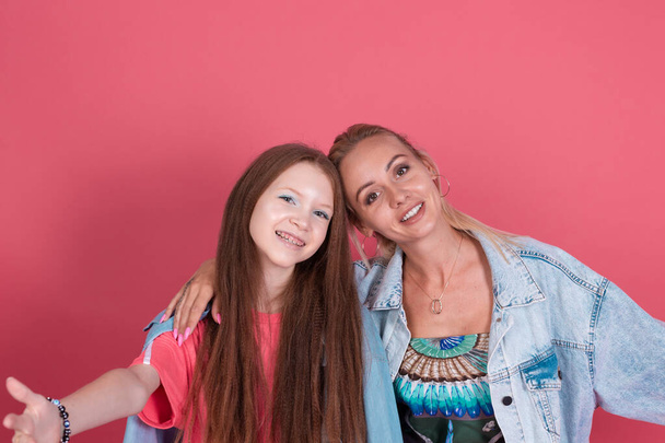 Modern mom and daughter in denim jackets on terracotta background hugging and smiling - Photo, Image