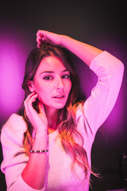 Young pretty woman in white sweater looking at camera with sweet eyes with pink and blue led lights - Fotografie, Obrázek