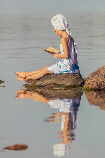 Young woman with a towel on her head at the sea. Lady reads a book in the water. The concept of summer outdoor recreation, relaxation. reading - Foto, Imagen