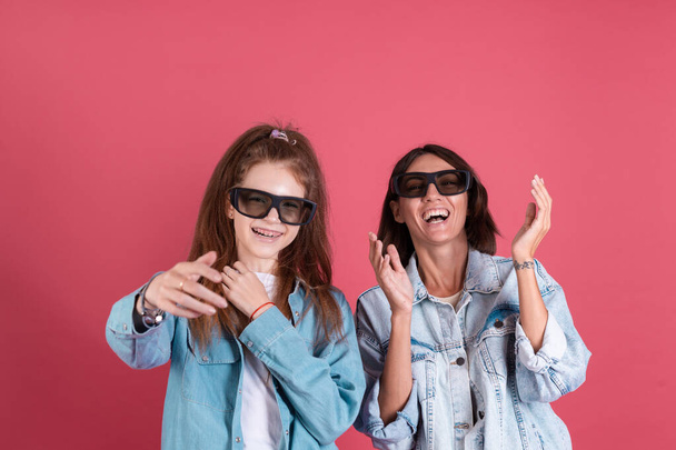 Moderna mamma e figlia in giubbotti di jeans su sfondo terracotta in 3 d occhiali cinema guardando film commedia insieme, sorridere e ridere - Foto, immagini