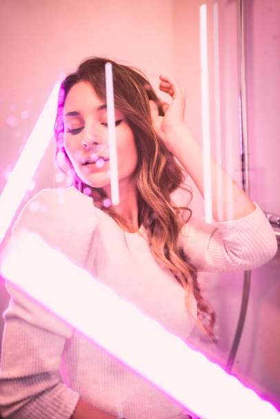 Beautiful young woman behind wet glass looking at camera with seductive gaze with pink led lights, vertical photo - Photo, Image