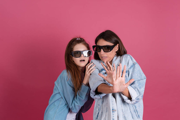 Moderní maminka a dcera v džínové bundy na terakotové pozadí ve 3D kinech brýle sledování horor film spolu, strach tvář - Fotografie, Obrázek
