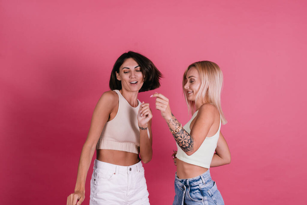 Zwei Freundinnen in lässig auf rosa Hintergrund, die zusammen Spaß haben, lächeln und lachen, Freundschaftskonzept - Foto, Bild