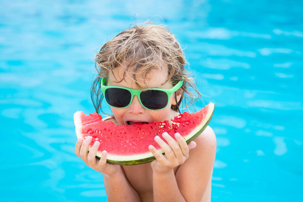 Kid with watermelon smiling swimming in pool on summer on resort. Children with piece of water melon outdoor. Summer vacation and healthy eating concept. - Foto, imagen