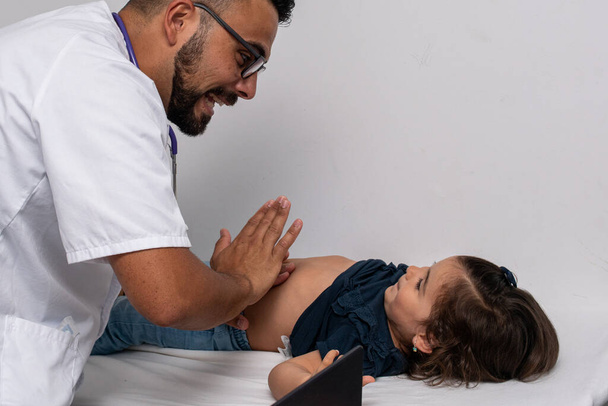 30χρονος καυκάσιος γιατρός εξετάζει τη μικρή του ασθενή, ένα 3χρονο κορίτσι.. - Φωτογραφία, εικόνα