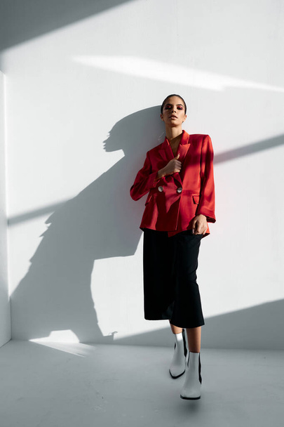 a woman in a red jacket and fashionable trousers leaned against the wall - 写真・画像