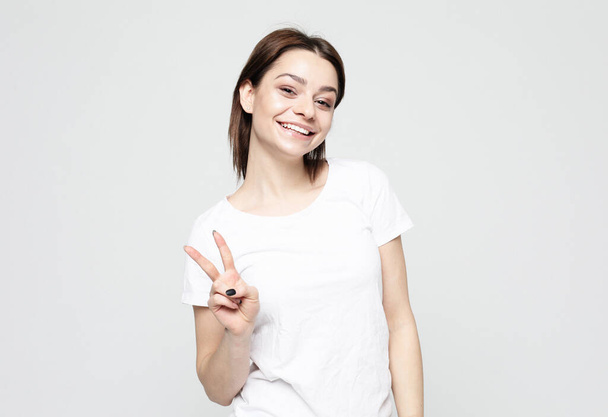 Young people, emotion and lifestyle concept: young woman with short hair wearing show victory sign over grey background - Φωτογραφία, εικόνα