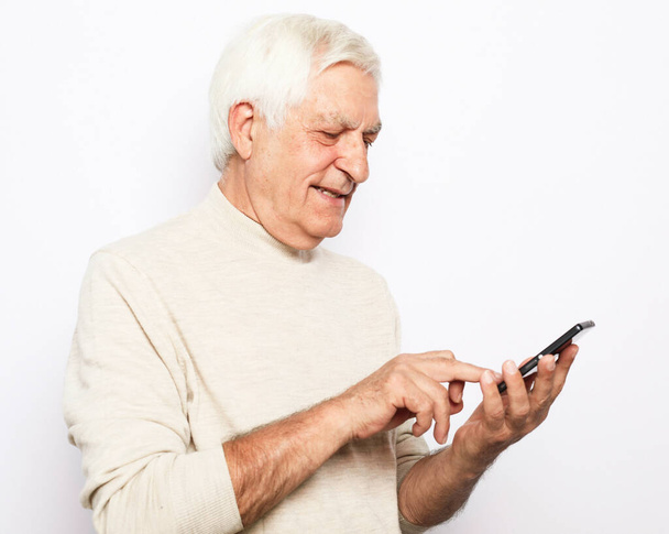 senior mężczyzna w casual strój radośnie uśmiechnięty i za pomocą nowoczesnego smartfona - Zdjęcie, obraz
