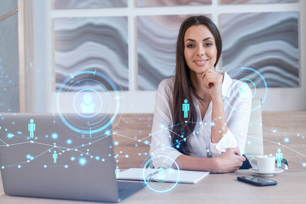 Attractive businesswoman in white shirt at workplace working with laptop to hire new employees for international business consulting. HR, social media hologram icons over office background - Photo, image