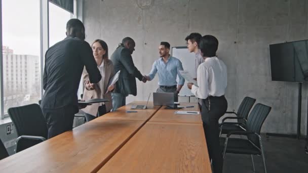 Мультирасовая группа коллег мультиэтнические корпоративные работники пожимают друг другу руки, пожимая приветственные жесты на совещании в офисе, садясь за стол слушания доклада латиноамериканского босса - Кадры, видео