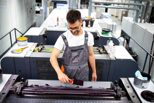 Profesjonalny operator maszyn drukarskich dodający więcej kolorów podczas procesu drukowania w fabryce. - Zdjęcie, obraz