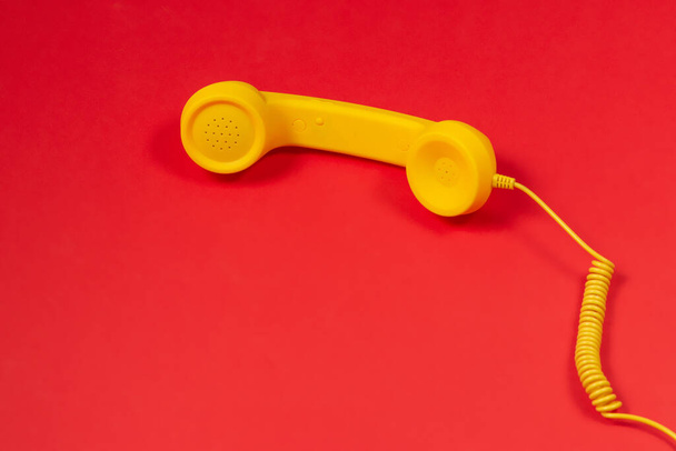 Желтый телефон на красном фоне.  - Фото, изображение