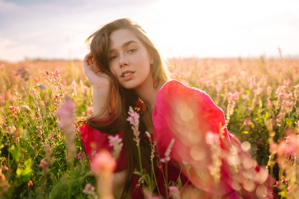 Stylish woman in a pink dress posing in the blooming field. Nature, vacation, relax and lifestyle. Fashion concept. - 写真・画像