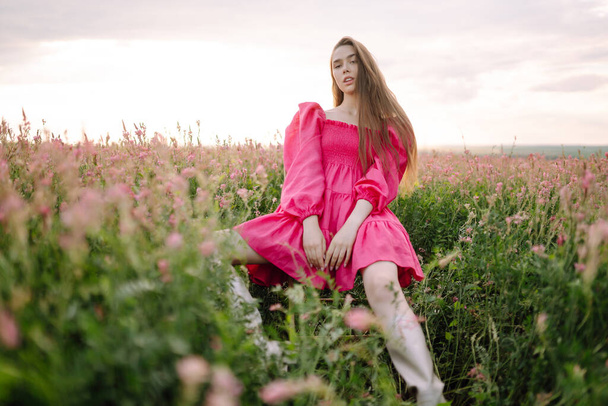 Stylish woman in a pink dress posing in the blooming field. Nature, vacation, relax and lifestyle. Fashion concept. - Fotografie, Obrázek