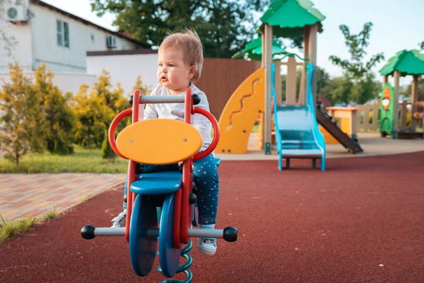 Adorable baby playing on the playground, sitting on a wooden bike. Outdoors. Concept of autism and childhood. - Photo, Image