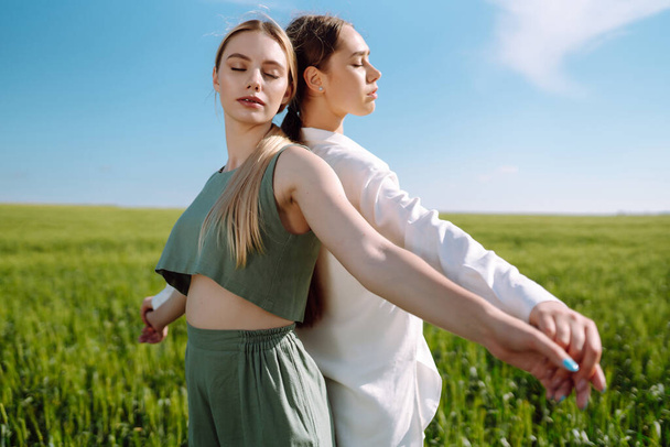 Portrait of two fair-haired girls in fashionable and stylish clothes, against the background of a field. Nature, vacation, relax and lifestyle. Fashion concept. - Photo, image
