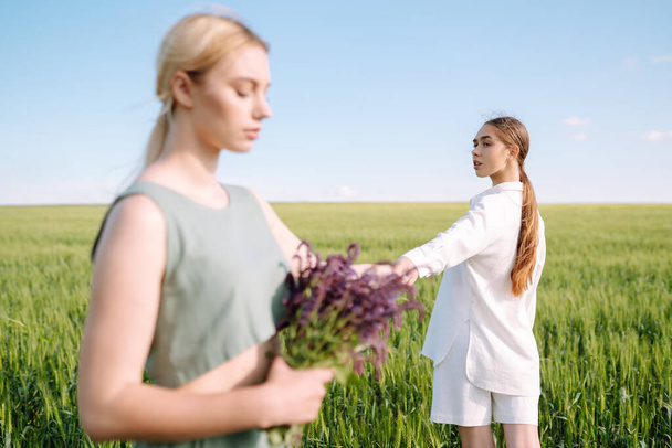 Portrait of two fair-haired girls in fashionable and stylish clothes, against the background of a field. Nature, vacation, relax and lifestyle. Fashion concept. - Фото, зображення