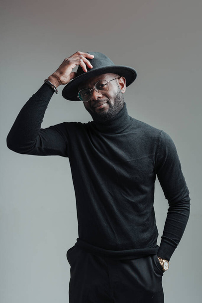 Handsome cute african american man wearing glasses in black turtleneck and hat holding her hand - Photo, image