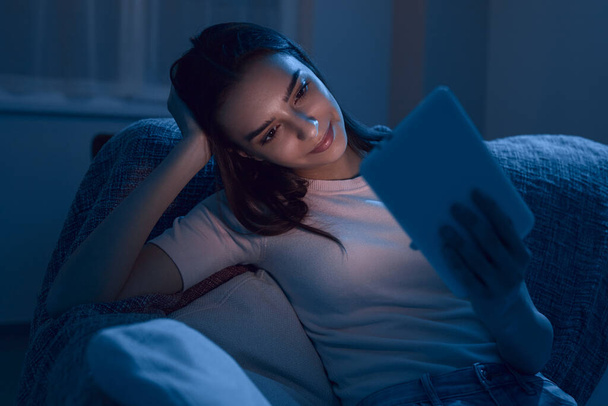 Smiling woman with tablet resting on sofa in evening - Photo, Image