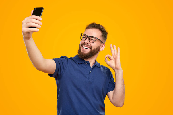 Happy bearded man showing OK sign and taking selfie - Foto, afbeelding