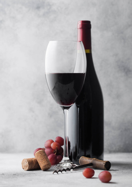Glass and bottle of red wine with corks and vintage corkscrew with grapes on light tabel background. - Foto, afbeelding