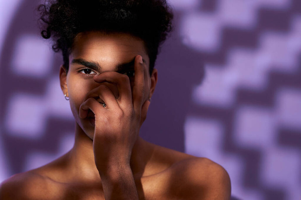 Close-up portret van fit mannelijk model poseren in de schaduw op paarse achtergrond. Transgender jongeman - Foto, afbeelding