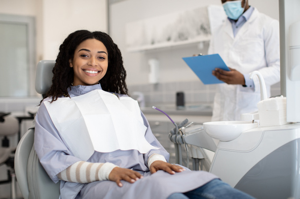 Glückliche junge Afrikanerin sitzt bei Termin in Stomatologischer Klinik auf Stuhl - Foto, Bild