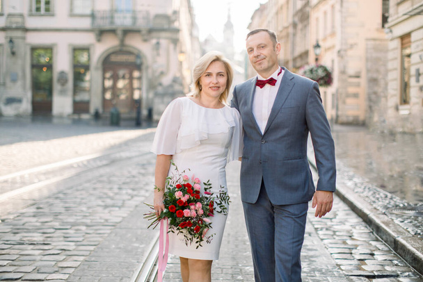 Mature couple in elegant fashionable clothes, walking in the street of old European city - Foto, afbeelding