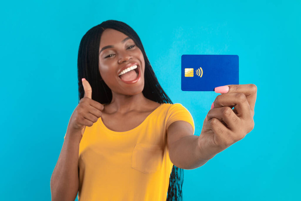 African American Woman Showing Credit Card Gesturing Thumbs-Up, Blue Background - Photo, Image
