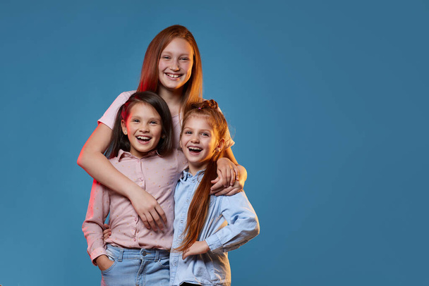 three kids girls standing together on blue background - Fotoğraf, Görsel