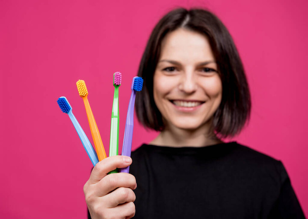 Beautiful happy young woman with different colored toothbrushes on blank pink background - Photo, image