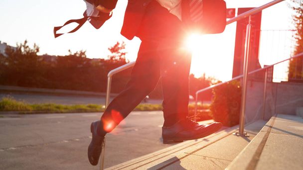 LENS FLARE: nierozpoznawalny mężczyzna w formalnych ciuchach pędzi po schodach o zachodzie słońca. - Zdjęcie, obraz
