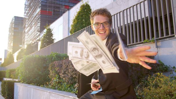 SUN FLARE, PORTRAIT: Happy businessman throws a bunch of money at the camera. - Foto, imagen