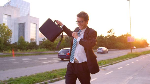 CLOSE UP: Carefree businessman dances along asphalt sidewalk on sunny evening. - Фото, изображение