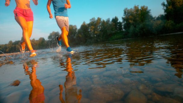Nízký úhel: Nerozpoznatelní tréninkoví partneři běžící v klidné řece. - Fotografie, Obrázek