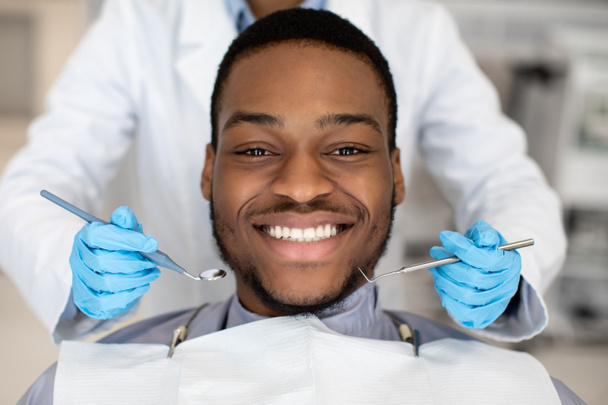 close-up van gelukkig zwart man patiënt krijgen tandheelkundige behandeling in moderne kliniek - Foto, afbeelding