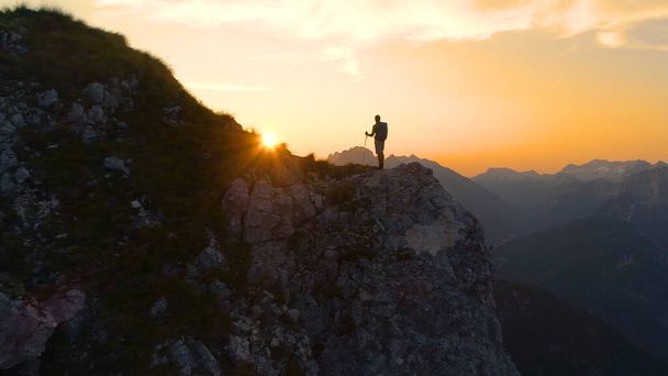 FLARE DE LA LENTE: Impresionante puesta de sol ilumina los Alpes y el excursionista de pie sobre un acantilado
. - Foto, imagen