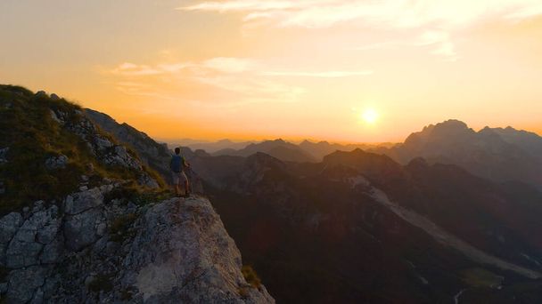 AERIAL Unrecognizable hiker stands on a cliff and observing the golden landscape - Foto, imagen