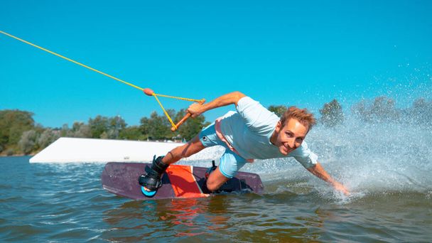 CHIUDI: Bello uomo wakeboarding fa una mano trascinare e spruzza acqua. - Foto, immagini