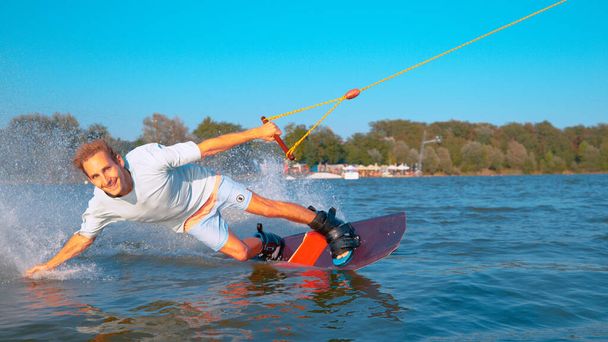 Κοντινό πλάνο: χαρούμενος άνθρωπος wakeboarding και πιτσίλισμα το νερό της λίμνης με το χέρι του. - Φωτογραφία, εικόνα