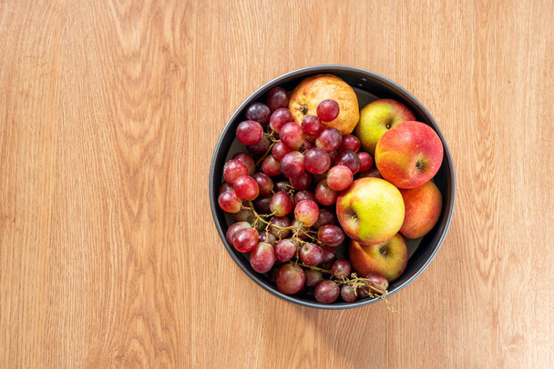 tigela de frutas visto a partir do topo com uvas vermelhas, maçãs vermelhas e romã em carvalho colorido fundo - Foto, Imagem