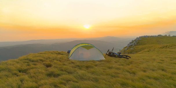 AERIAL: Flying behind an empty tent sitting in the meadow at beautiful sunset. - Photo, image
